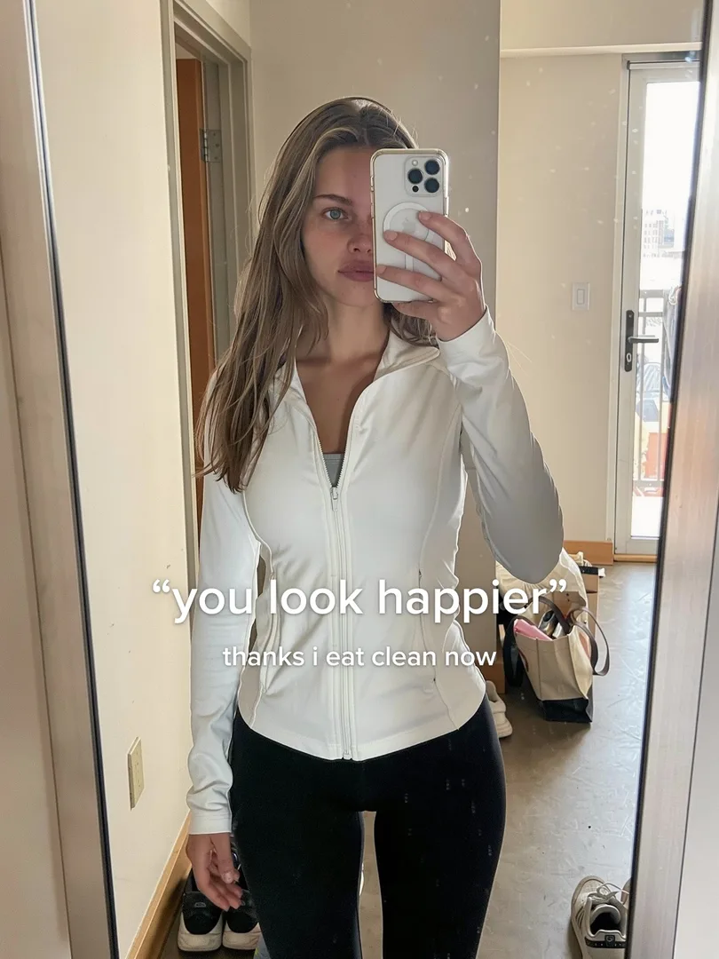 Mirror selfie of a young woman in a white zip jacket, text: you look happier, thanks i eat clean now