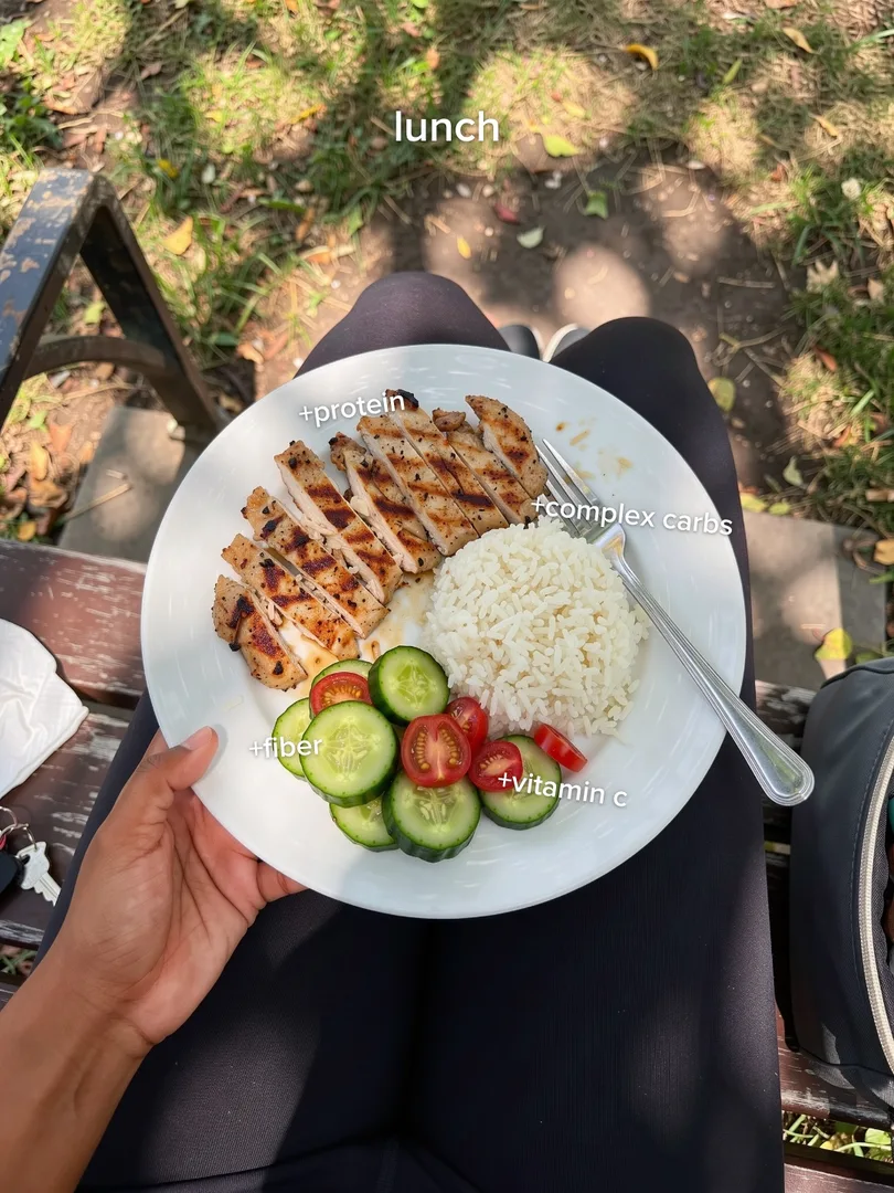Lunch plate on a lap: grilled chicken, rice and cucumber, with plus-protein labels