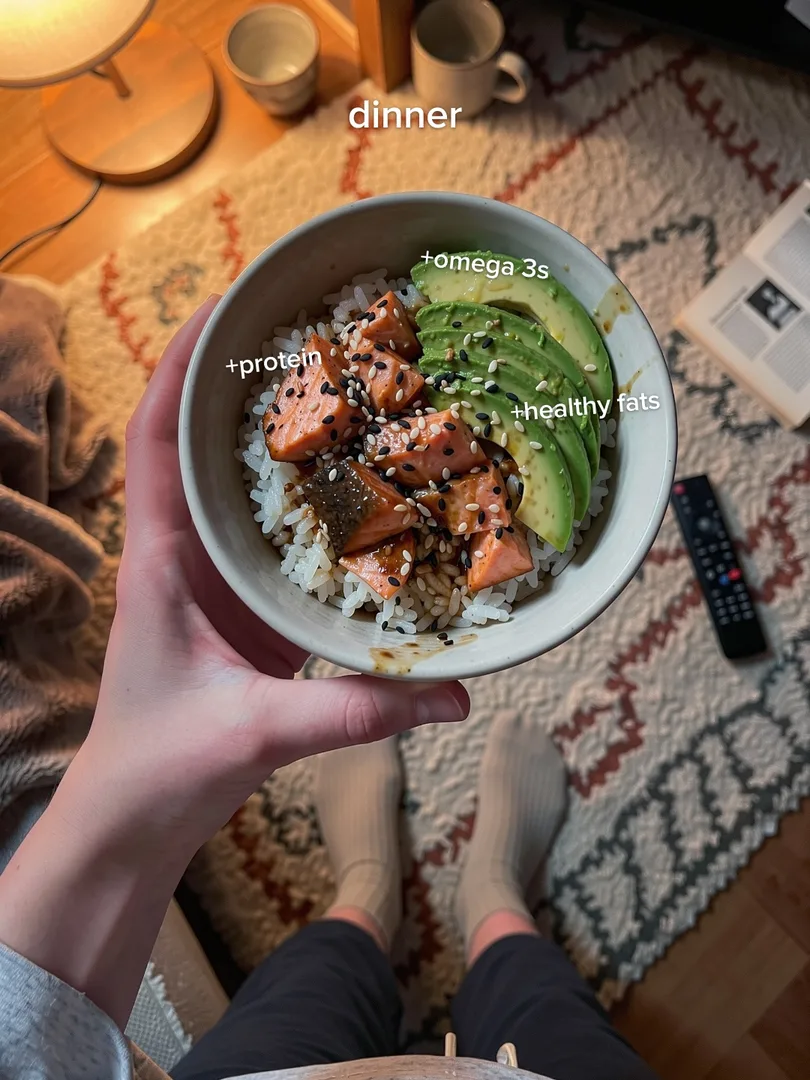 Salmon and avocado rice bowl held over a rug, labels omega 3s and healthy fats