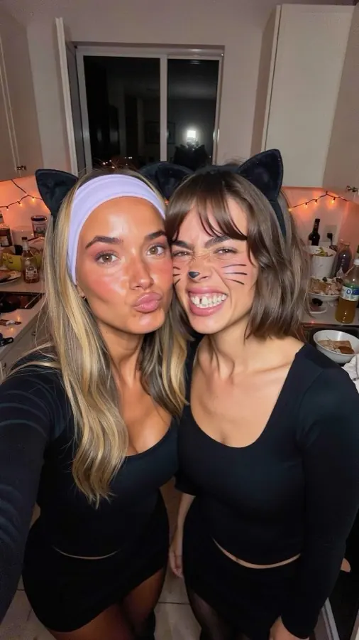 Two friends in cat ears taking a selfie in a kitchen at a Halloween party