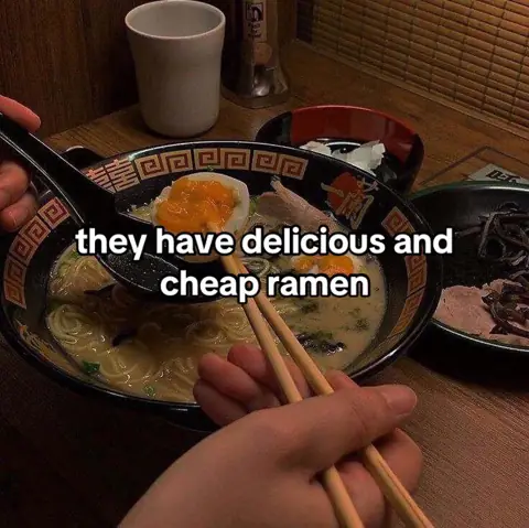 A hand holding chopsticks over a bowl of ramen in a booth